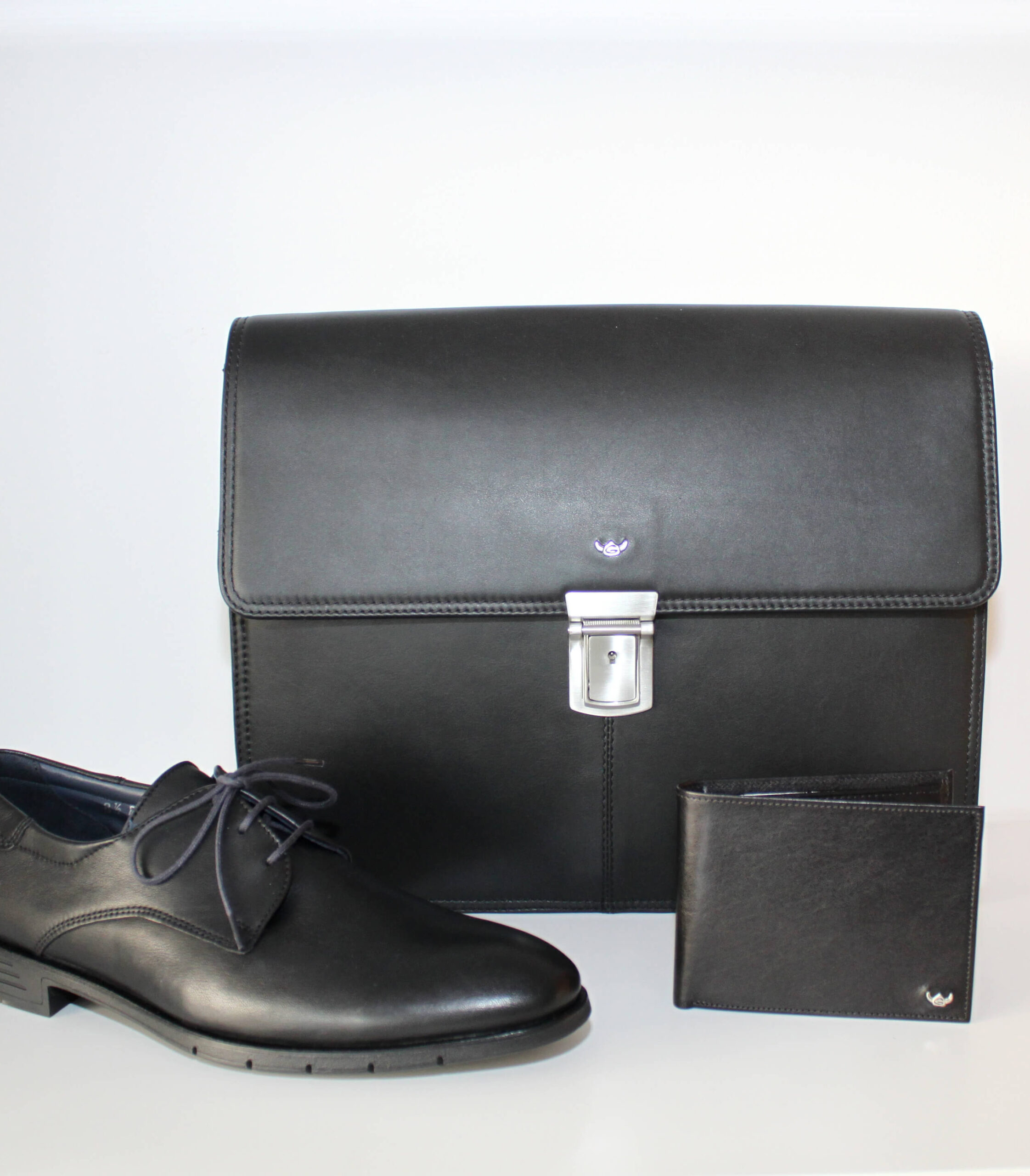 Schwarze Leder Tasche steht im Hintergrund und davor ein schwarzer Anzugsschuh und eine Brieftasche