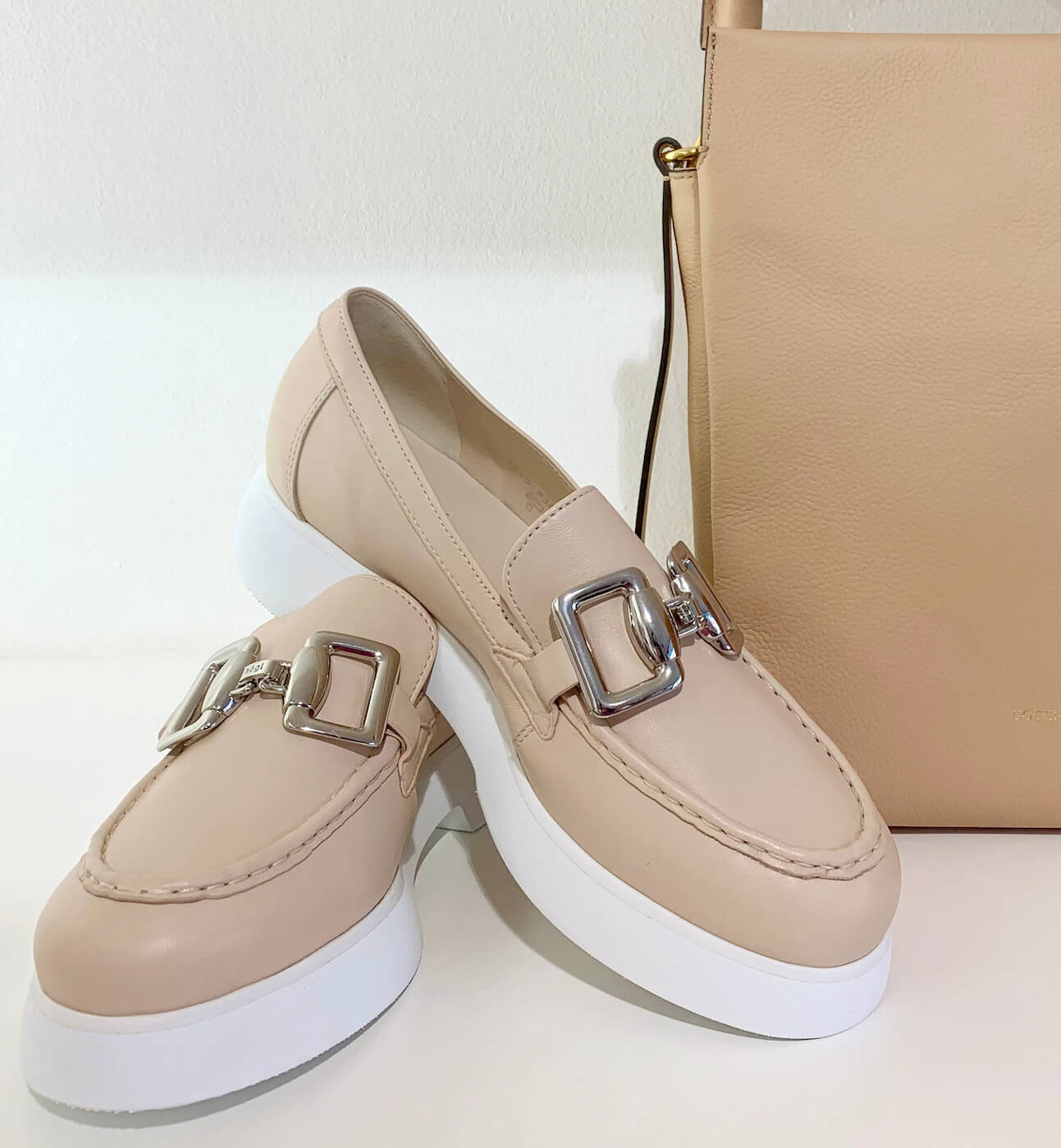 Beige Schuhe mit einer silbernen Schnalle und im Hintergrund steht eine Tasche